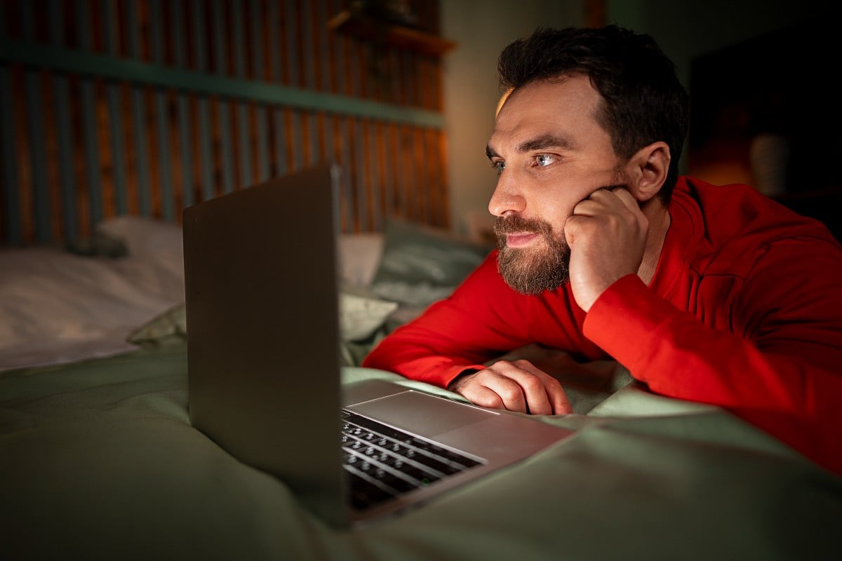 Un uomo guarda pornografia online nel suo letto.
